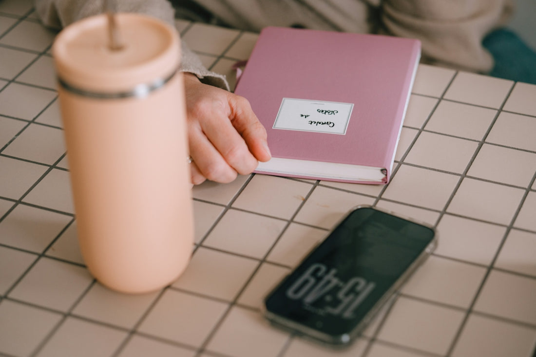 A pink tumbler, book, and phone on a checkered surface